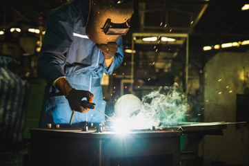 Industrial worker welding metal with many sharp sparks