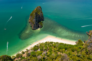 Aerial drone view of a beautiful tropical sandy beach surrounded by green jungle and towering...