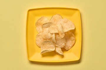 Potato chips on plate, minimal. Vegan beer snack on yellow background. Crispy veggie chip, creative monochrome yellow concept. Home made potato crisps, top view