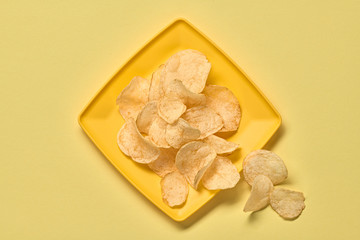 Potato chips on plate, minimal. Vegan beer snack on yellow background. Crispy veggie chip, creative monochrome yellow concept. Home made potato crisps, top view