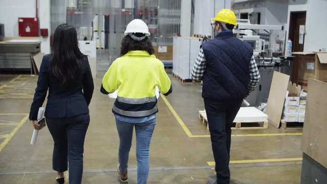 Back view of factory workers walking at plant. Rear view of people walking with blueprints at printing house. Print manufacturing concept