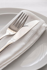 Silver fork and knife with white linen napkin on the plate. Restaurant dinning concept. Close up of detail