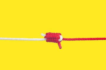 Red and White ropes tied together on yellow background. Unity power concept