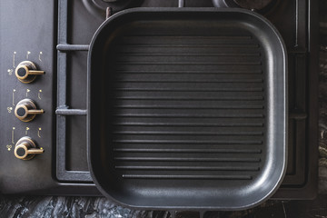 Grill pan rectangular shape, non-stick coating and several parallel protrusions on a gas stove.