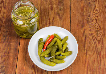 Pickled gherkins on saucer and in jar on rustic table