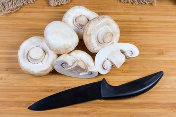 Fresh uncooked button mushrooms and ceramic knife on cutting board