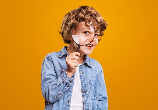 Naklejki Cheerful boy with magnifying glass looking at camera