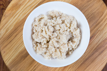 Barley porridge in bowl on wooden serving board, top view