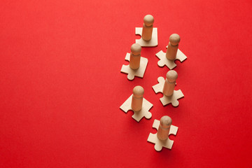 Obraz premium Wooden figures on puzzles on red background as a symbol of team building. Organization group people in business. Cooperation and partnership.