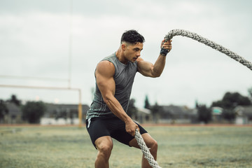 Strong man exercising with battle ropes on a field