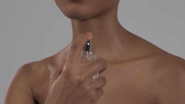 Close-up of a young beautiful African woman spraying perfume on herself. Isolated on a white background