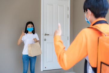 Asian woman pick up delivery food bag from door knob and thumb up form contactless or contact free from delivery rider with bicycle in front house for social distancing for infection risk.