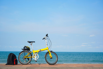 A yellow bicycle parking by the beach.  Helmet & backpack at the back and the bike.  Sports, recreation, travel, tourism including park and outdoor categories.