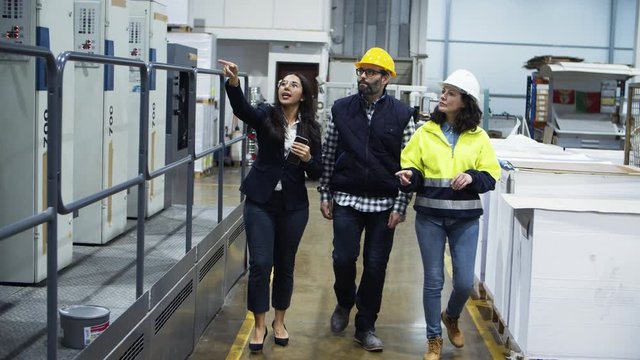 Front view of factory workers walking and talking at plant. Confident young project manager showing new five-section offset machine to technicians. Industry concept
