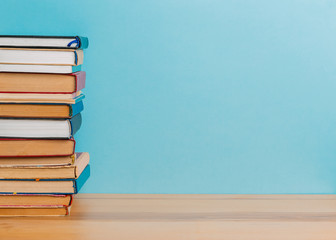 A simple composition of many hardback books, raw books on a wooden table and a bright blue background. Going back to school. Copy space. Education.