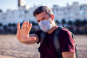 Man with medical mask showing stop gesture outdoor. People, healthcare and medicine concept