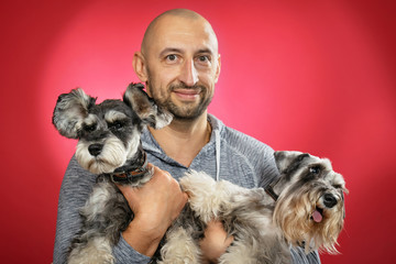 Two schnauzer dogs in the arms of a smiling man