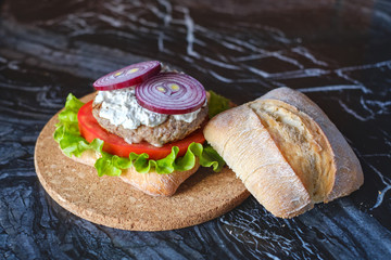 Homemade burger with beef chop, tomato, lettuce and dorblu blue cheese sauce. Serve on a wooden kitchen board on a table made of natural stone. Background image.