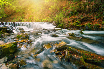 Fototapeta na wymiar Waterfall on a mountain river in the autumn forest under bright sun