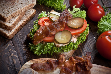 sandwich with smoked meat, green salad, fresh tomatoes and pickled cucumbers, on kitchen wooden table background