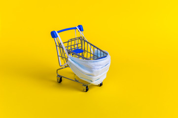 Blue shopping cart with medical mask for virus protection on yellow background. Creative concept of healthcare and safe shopping on coronavirus quarantine © Julia Lavrinenko