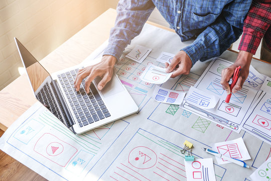 close up male asian ui/ux designers working and designing a user interface for website and application, working together with partner planning and brainstorming sketch designs with computer laptop