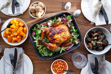 Top view of decorated festive table with whole roasted chicken, salad, pumpkin, mushrooms, beans and walnut. The concept of family dinner or Thanksgiving celebrate.