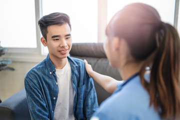 beautiful female doctor smiling and placing hand onto male patients shoulder in comfort, help and support. Diagnosing patient and explaining their health issues and problems, within a hospital office