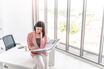beautiful female asian worker holding a folder file of documents and information on work or business looking, reading, learning from the documents, while holding a pen working in an office environment