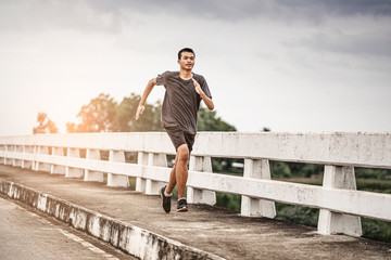 asian teenager running along the bridge in sprinting action, exercising or practicing for a...