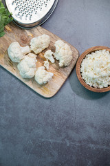Cauliflower, cauliflower rice and grater on concrete background. Vertical picture. Top view.
