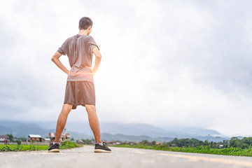 asian teen stretching his body and running along the road, exercising or practicing for a marathon race, wearing shirt, short and trainers with mountain nature and cloudy sunset sky in the background