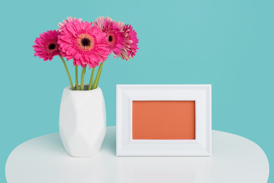 Happy Mother's Day, Women's Day, Valentine's Day or Birthday Background. Beautiful dark pink gerbera daisies in a vase and an empty picture frame greeting card.