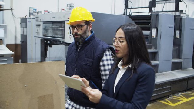 Focused project manager giving instructions to mature engineer. Two factory workers walking at plant with tablet. Industry, technology concept