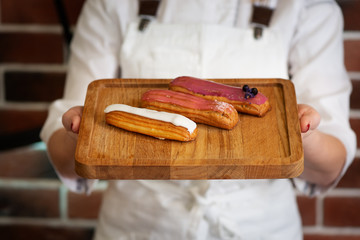 The confectioner in gloves makes eclairs with cream