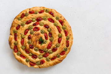 Homemade italian flat bread - Focaccia contorta. With olives, olive oil, rosemary, tomatoes. Traditional recipe. Vegan. White concrete texture background.