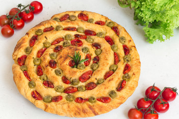 Homemade italian flat bread - Focaccia contorta. With olives, olive oil, rosemary, tomatoes. Traditional recipe. Vegan. White concrete texture background.