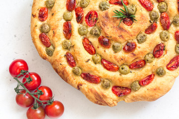 Homemade italian flat bread - Focaccia contorta. With olives, olive oil, rosemary, tomatoes. Traditional recipe. Vegan. White concrete texture background.