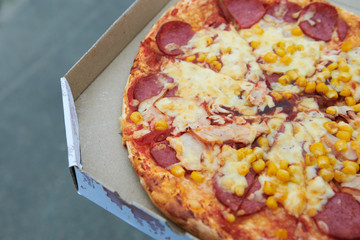Fresh appetizing pizza with corn salami and double cheese. Pizza in the box outdoor. Meat pizza with ham. Closeup.