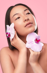 Young woman with clean skin touching face with flowers - obrazy, fototapety, plakaty