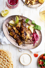 Chicken tikka kebab with red onion, coriander and fresh salad. Traditional indian dish made of chicken marinated in yoghurt and spices. Creative flatlay on white wooden background.
