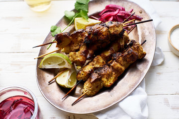 Chicken tikka kebab with red onion, coriander and fresh salad. Traditional indian dish made of chicken marinated in yoghurt and spices. Creative flatlay on white wooden background.