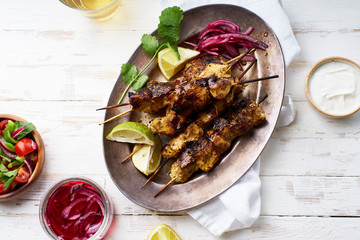 Chicken tikka kebab with red onion, coriander and fresh salad. Traditional indian dish made of chicken marinated in yoghurt and spices. Creative flatlay on white wooden background.
