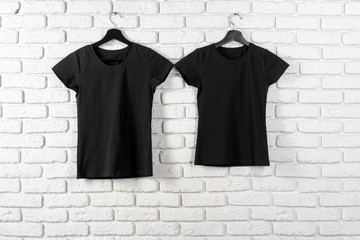 Black t-shirt hanging on a hanger against brick wall, front view