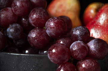 purple grapes and ripe pear fruits on dark plate, no people
