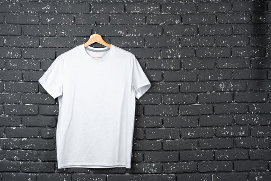 White t-shirt hanging on hanger against brick wall, copy space