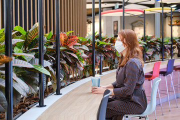 A woman in a medical mask sits at a table in a cafe