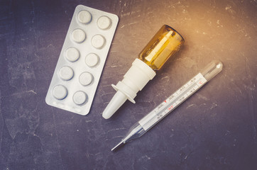 Drug spray bottle, pills packages and thermometer on black background/Drug spray bottle, pills packages and thermometer. Medicine subject. Top view.