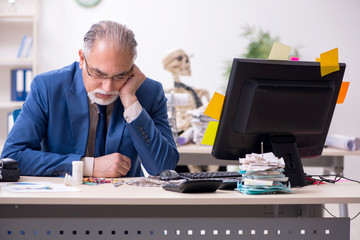 Old male sick employee working overtime in the office