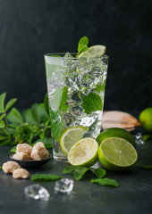 Glass of Mojito cocktail with ice cubes mint and lime on black board with fresh limes and cane sugar with wooden squeezer.